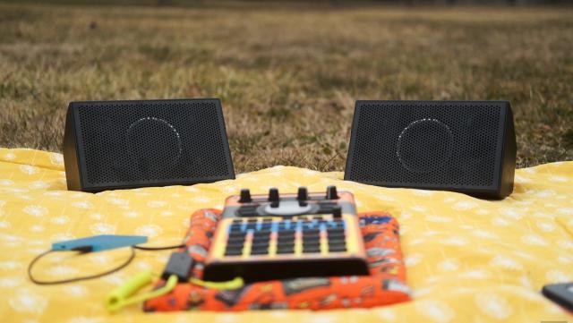 AIAIAI Unit 4 Wireless+ studio monitors on a picnic blanket in a park along with an SP-404 MKII with an adorable Speak & Spell skin.